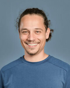 Freundlicher Mann mit langen Haaren und schönem Lächeln, trägt einen blauen Pullover, moderner Lifestyle, positive Energie, natürliche Ausstrahlung, professioneller Ausdruck, Wellness und Fitness, gesunde Lebensweise, positive Stimmung, portrait.