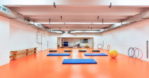 Bewegungsraum für Aqua Fitness mit blauen Matten, Gymnastikreifen, Gymballen und Fitnessgeräte in einem hellen, modern gestalteten Raum.