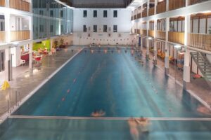 Innenaufnahme eines modernen Aqua-Fitness-Pools mit klarem Wasser, warmem Licht, Liegeflächen und Trainerbereichen, ideal für Wassertraining, Rehabilitation und Aquafitness in einem stilvollen Wellnesscenter.