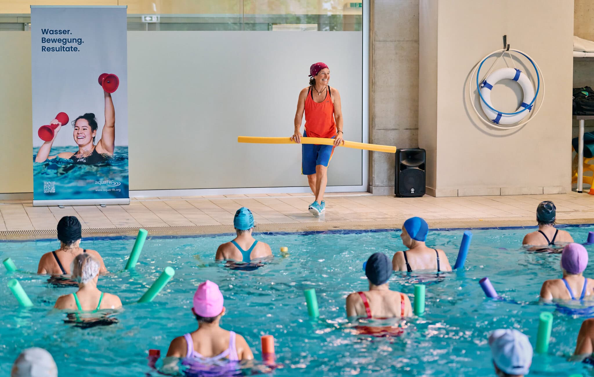 Aqua Fit Wassertraining mit Trainerin und Teilnehmern im Schwimmbad, inklusive Wasserhanteln und Pool-Accessoires, fördert Fitness und Gesundheit.